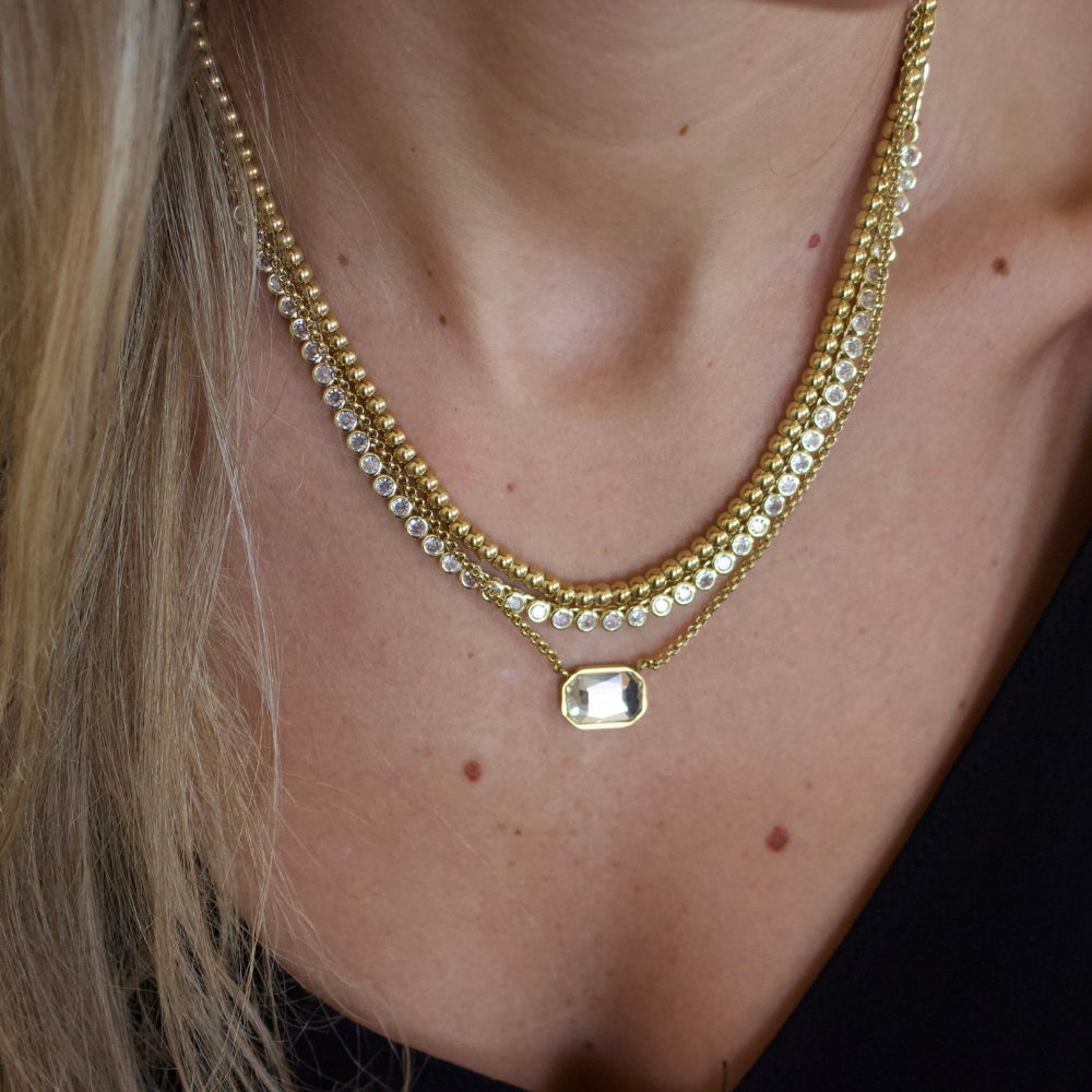 Close-up of a person wearing two gold necklaces with clear stones.