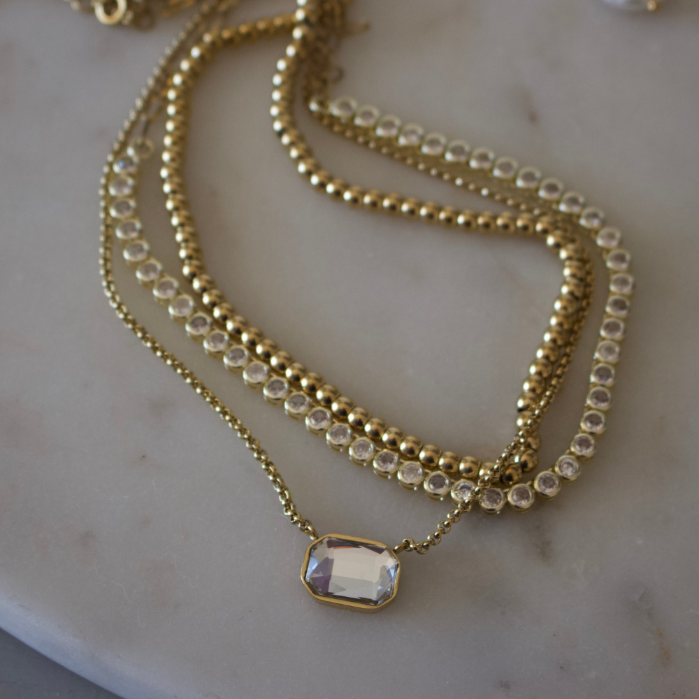 Gold necklace with a clear gemstone pendant on a marble surface