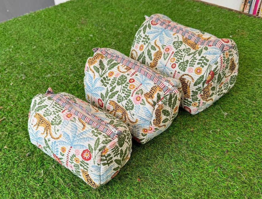 Three  quilted fabric cosmetic bags with a colorful animal leopard and floral pattern on a green grass-like surface.