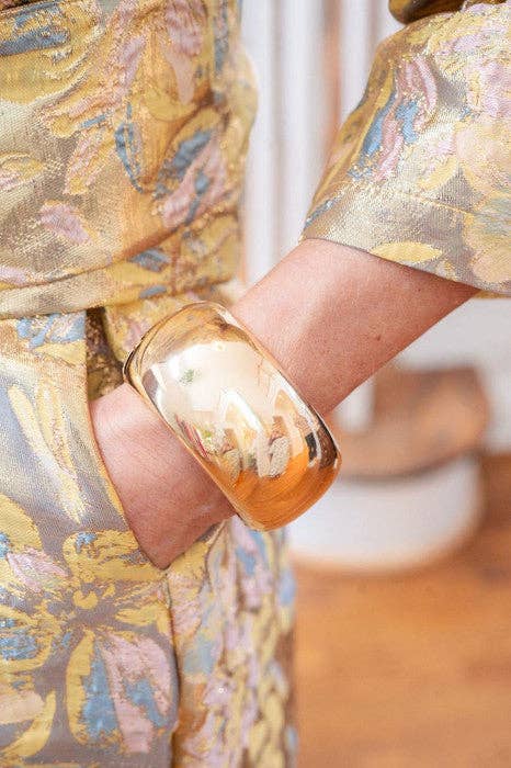 Close-up of a hand wearing a large gold bangle cuff 