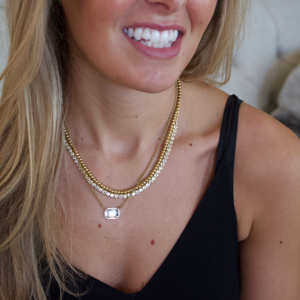 Close-up of a woman wearing a gold layered tennis necklace 