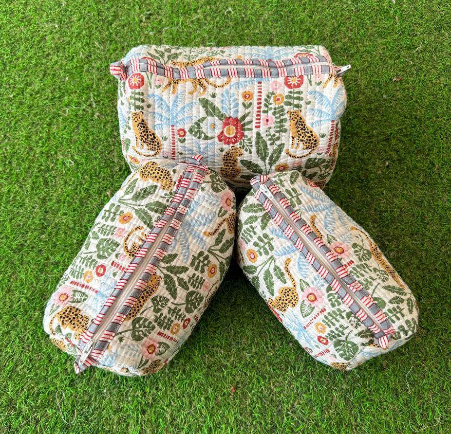 Three  quilted fabric cosmetic bags with a colorful animal leopard and floral pattern on a green grass-like surface.