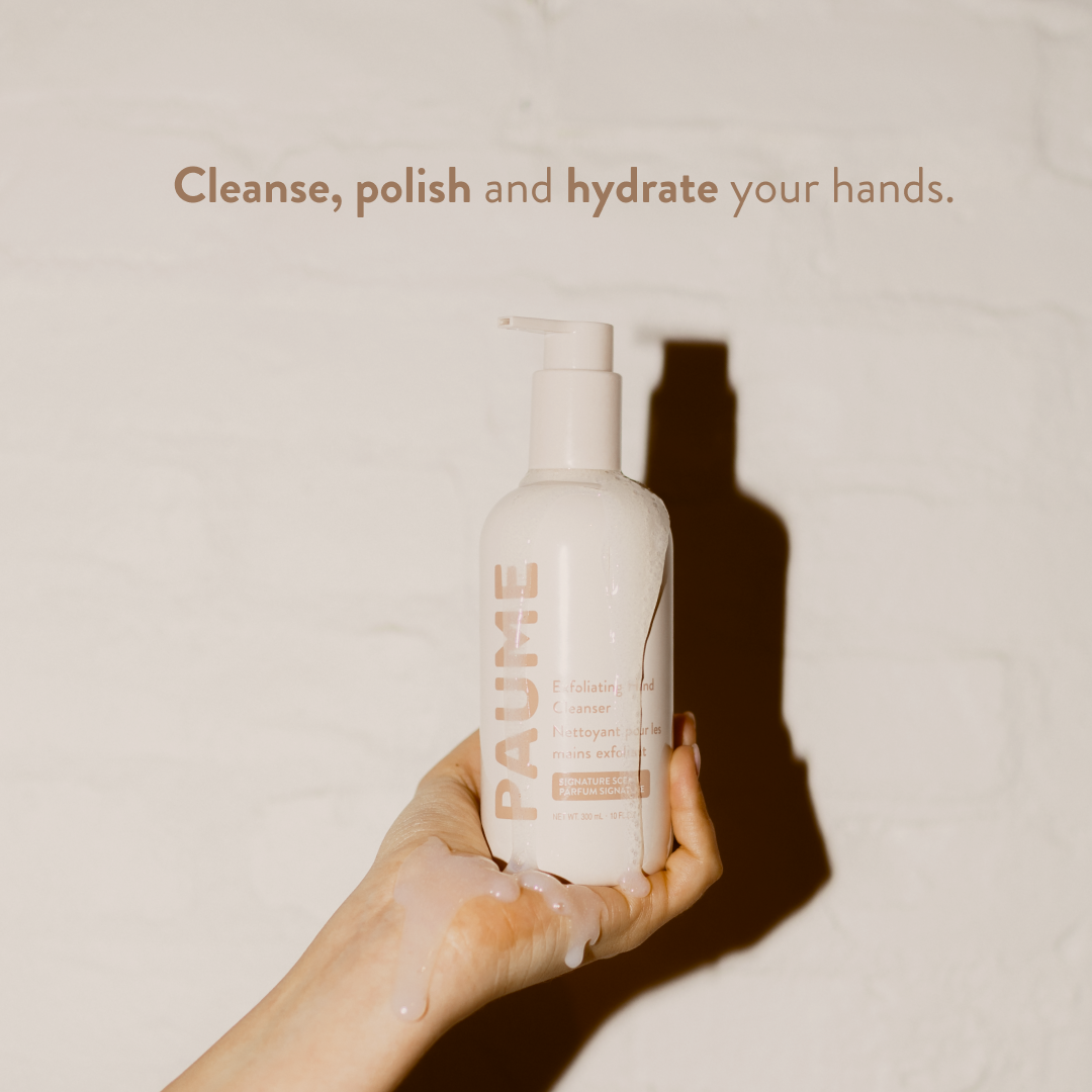 Hand holding a bottle of PAUME hand cream with text 'Cleanse, polish and hydrate your hands.' on a beige background