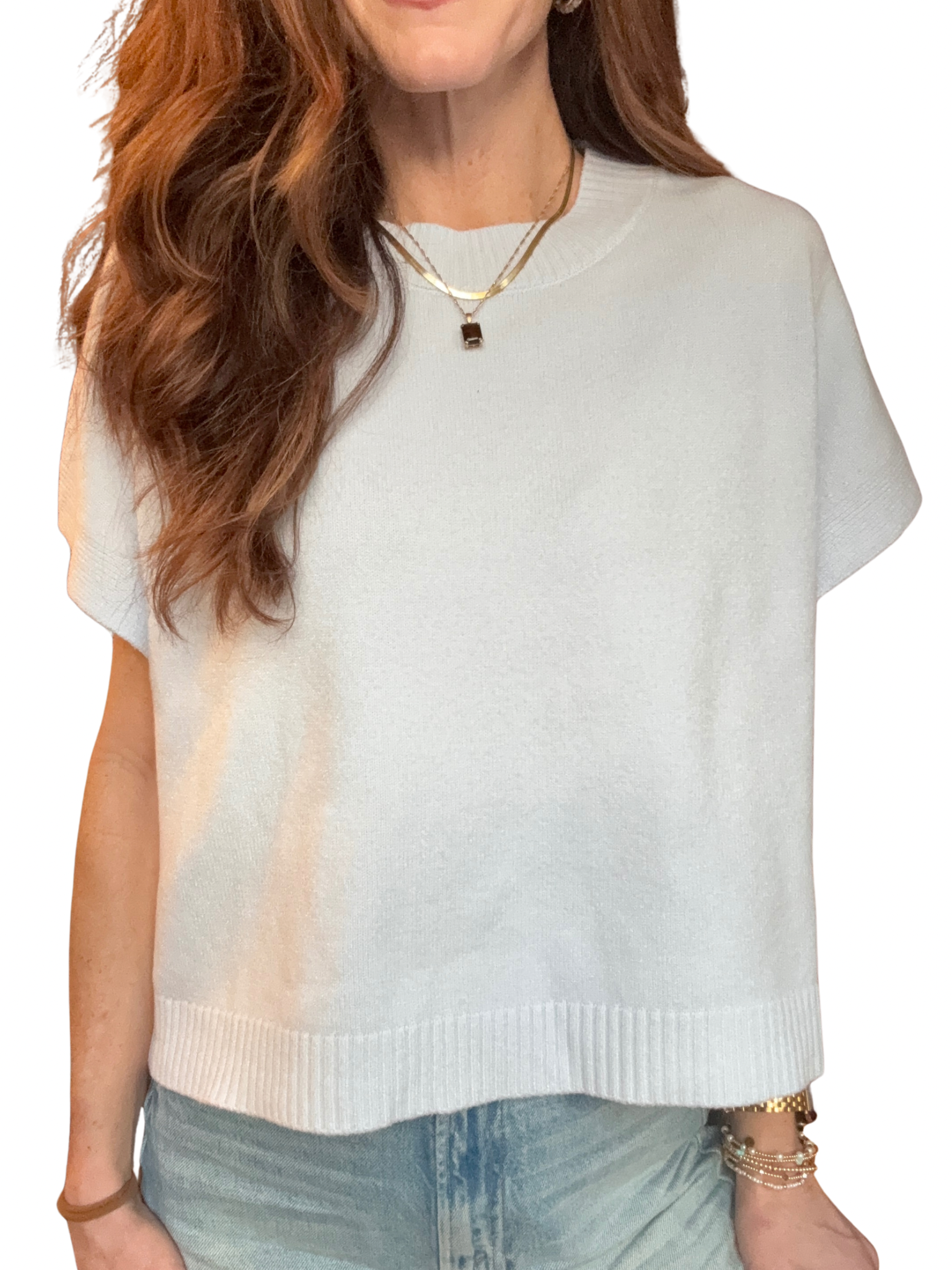 Woman wearing a light blue short sleeve sweater over a white shirt with denim shorts on a white background