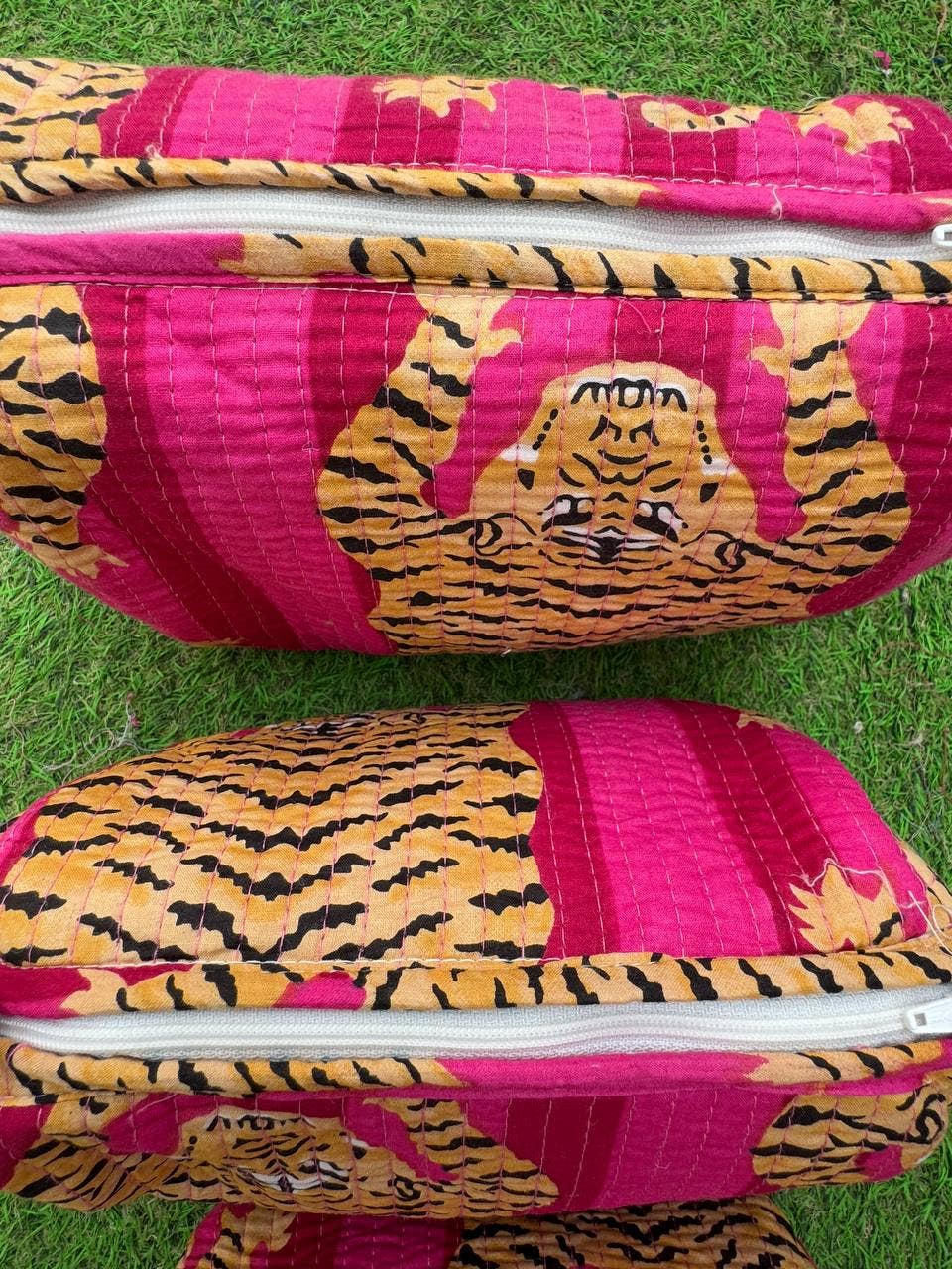 Two pink fabric toiletry bags with tiger pattern on a grass background