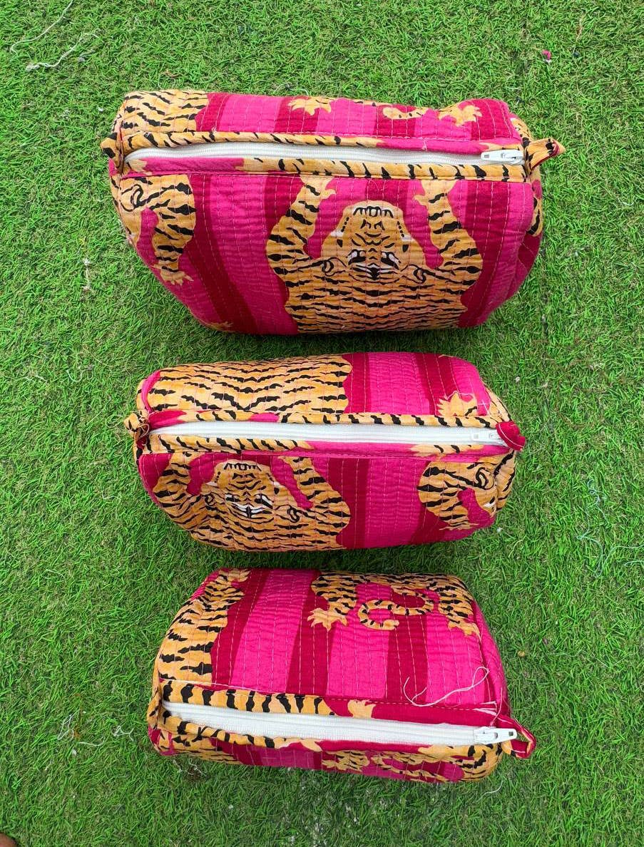 Three pink and orange tiger-patterned cosmetic toiletry pouches on a green grass background