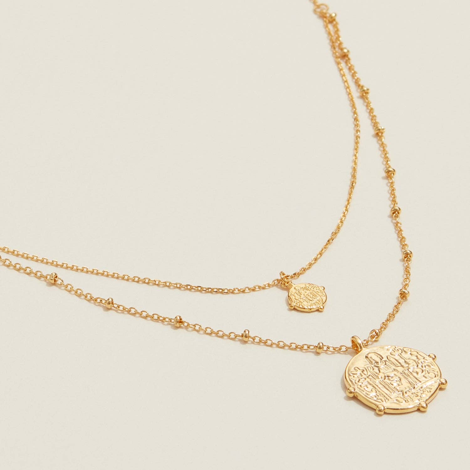 Gold necklace with two medallion pendants on a light beige background